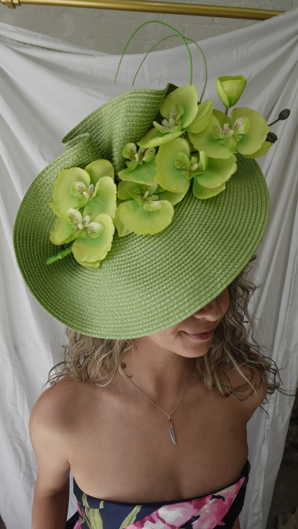 Person wearing a green straw hat with floral decorations, lying on a white surface.