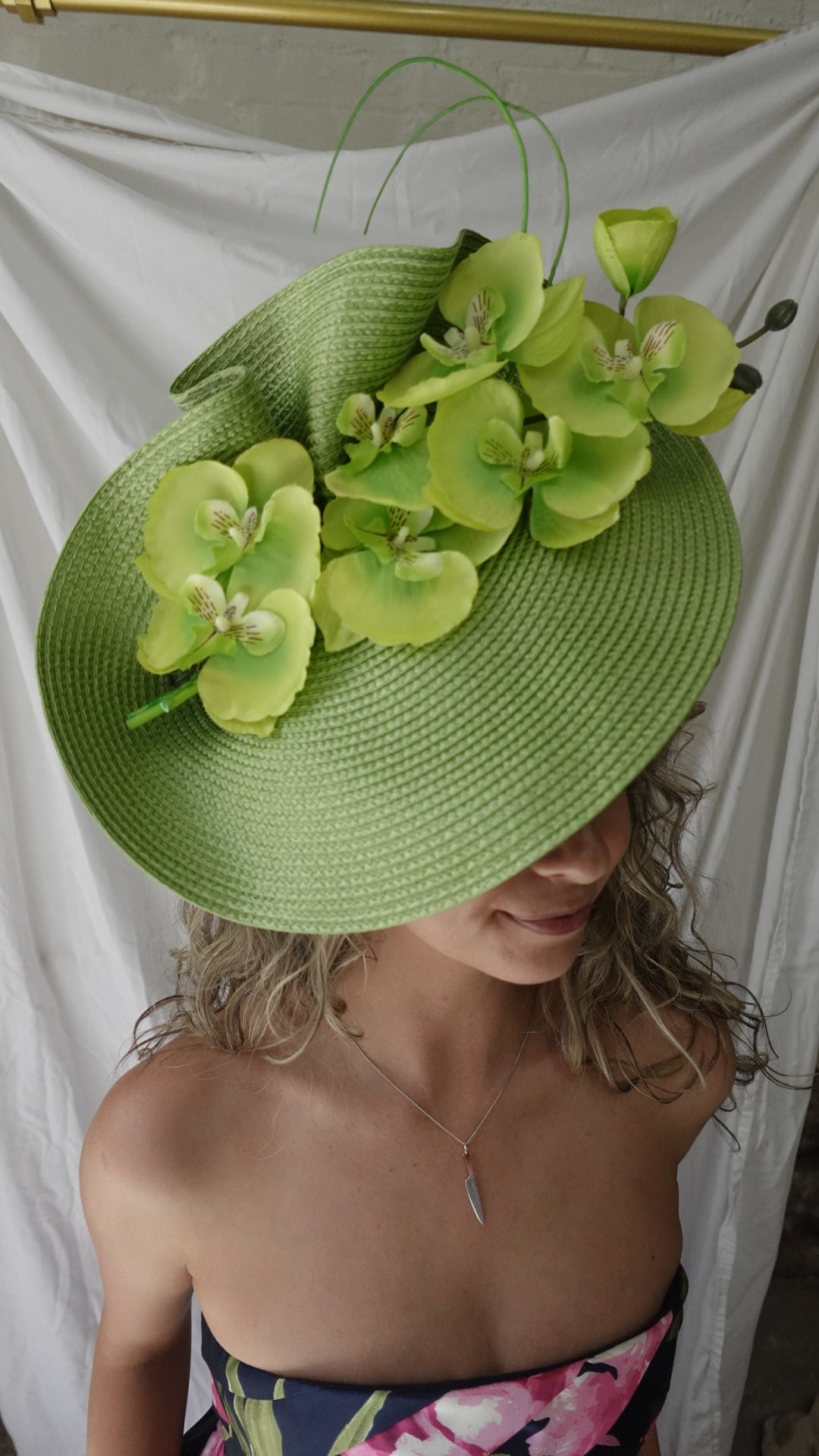 Person wearing a green straw hat with floral decorations, lying on a white surface.