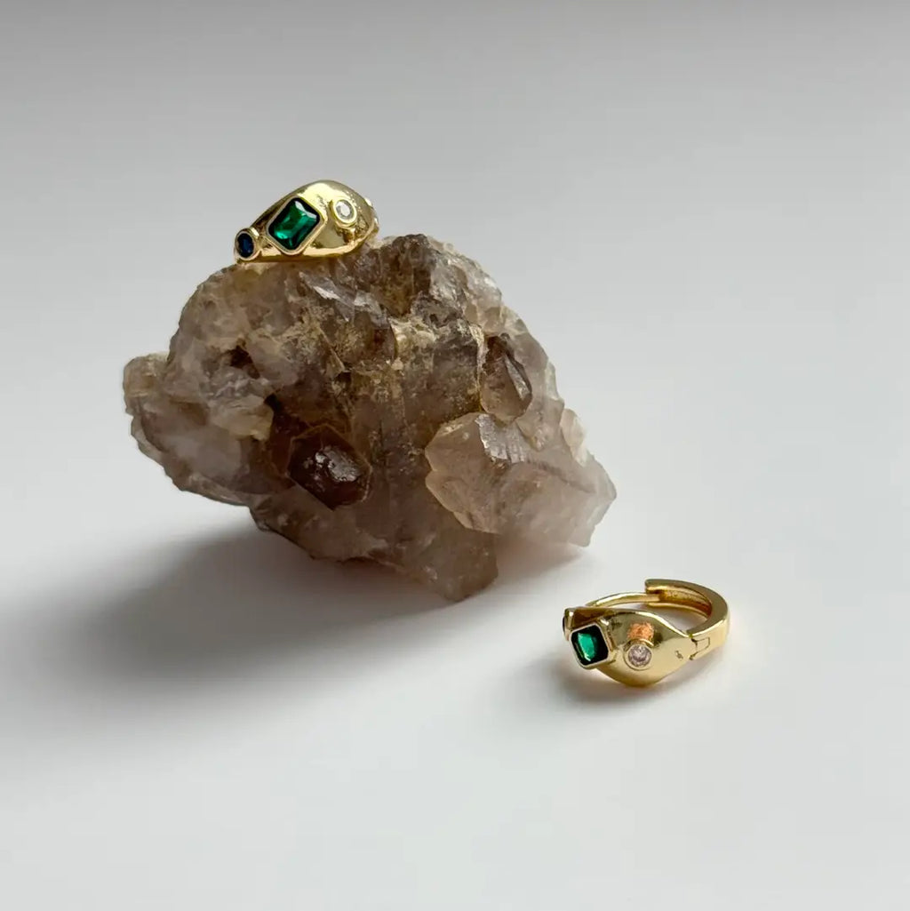 Gold ring with green gemstone on a crystal rock and plain background
