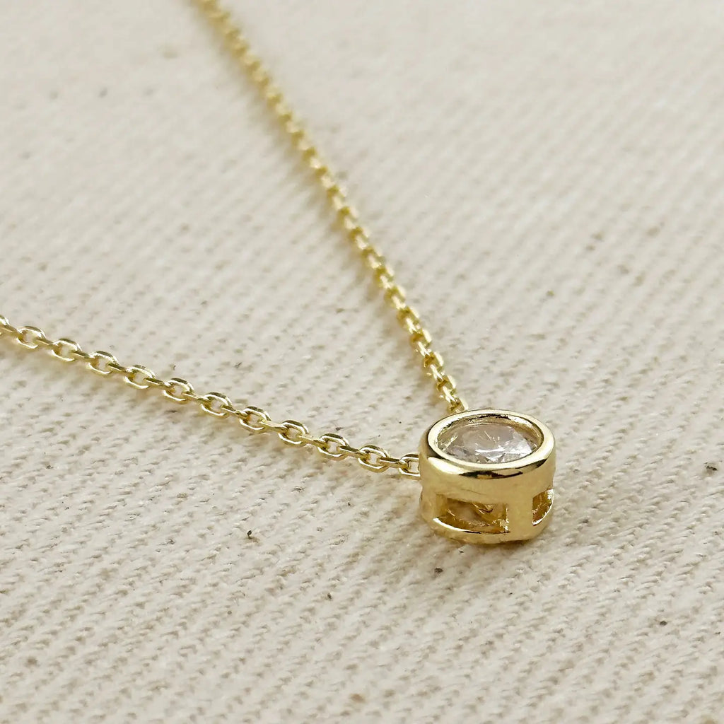 Gold necklace with a small round pendant on a textured beige surface