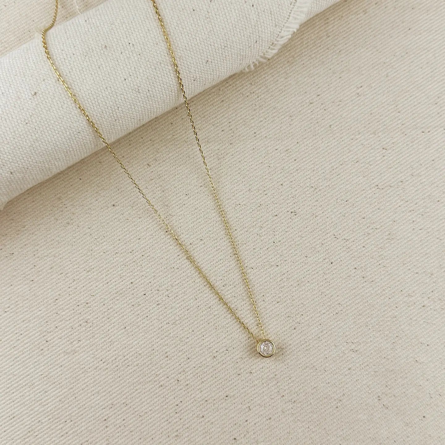 Delicate gold necklace with a small diamond pendant on a beige fabric background