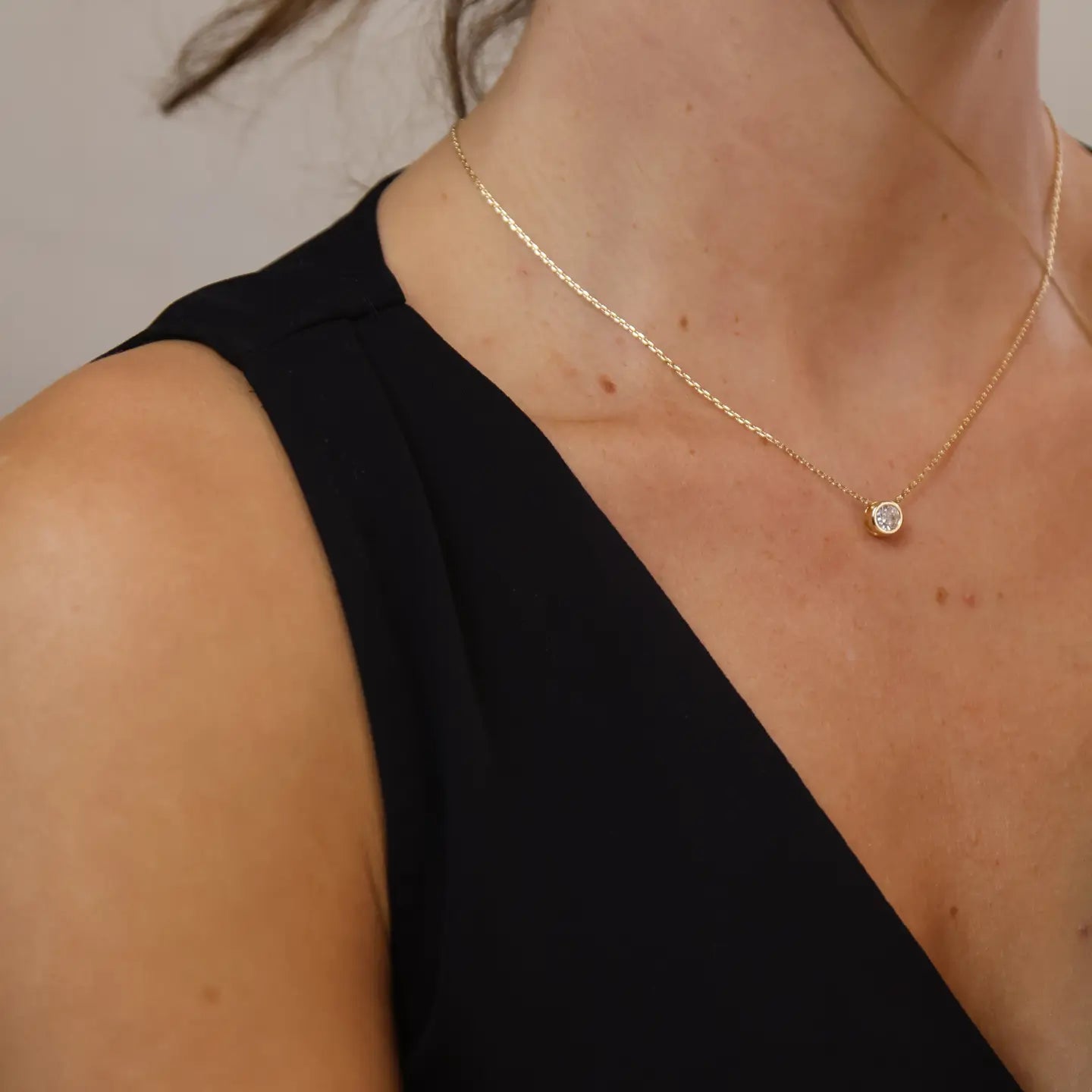 Gold necklace with a small round pendant on a person wearing a black top.