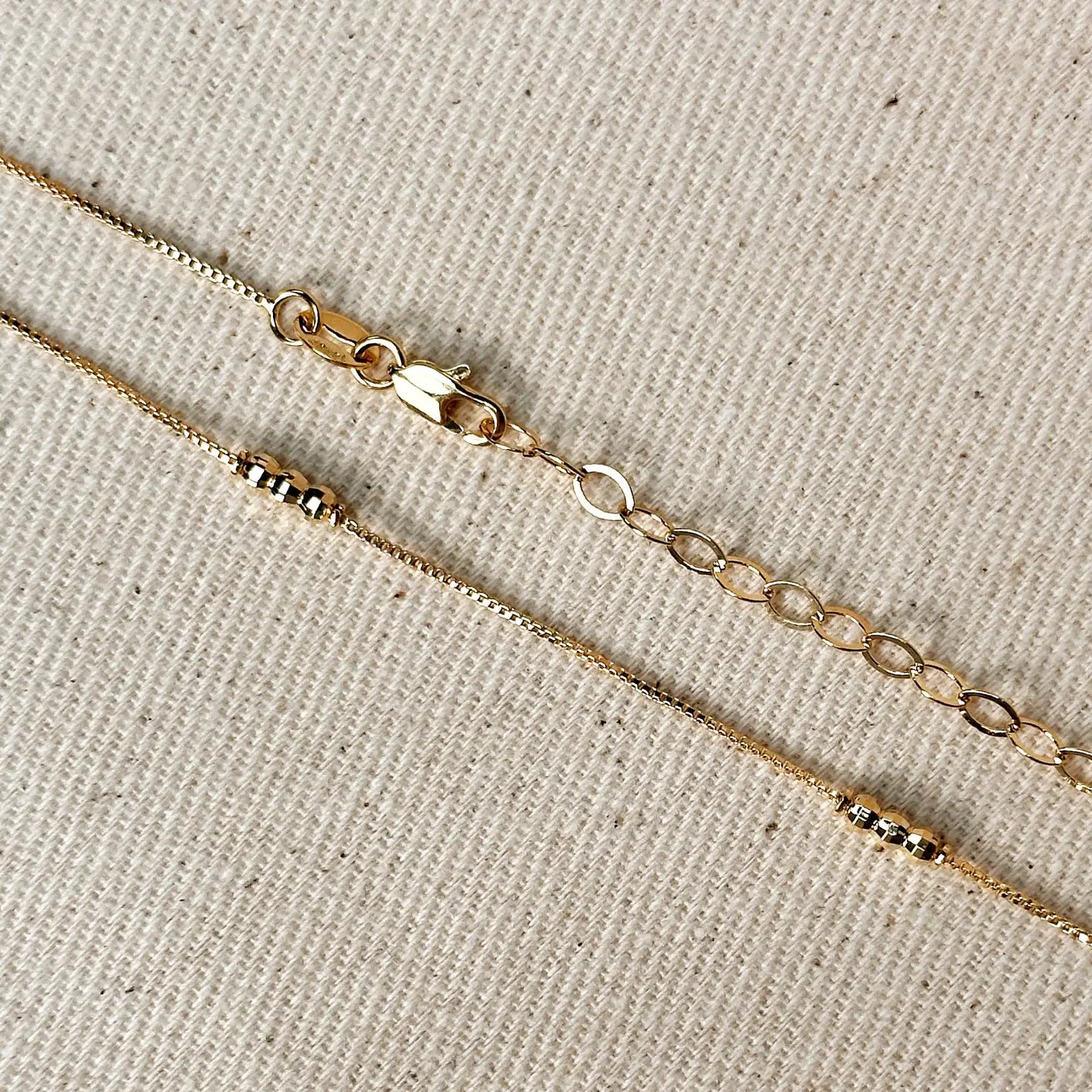 Two gold necklaces on a beige fabric background