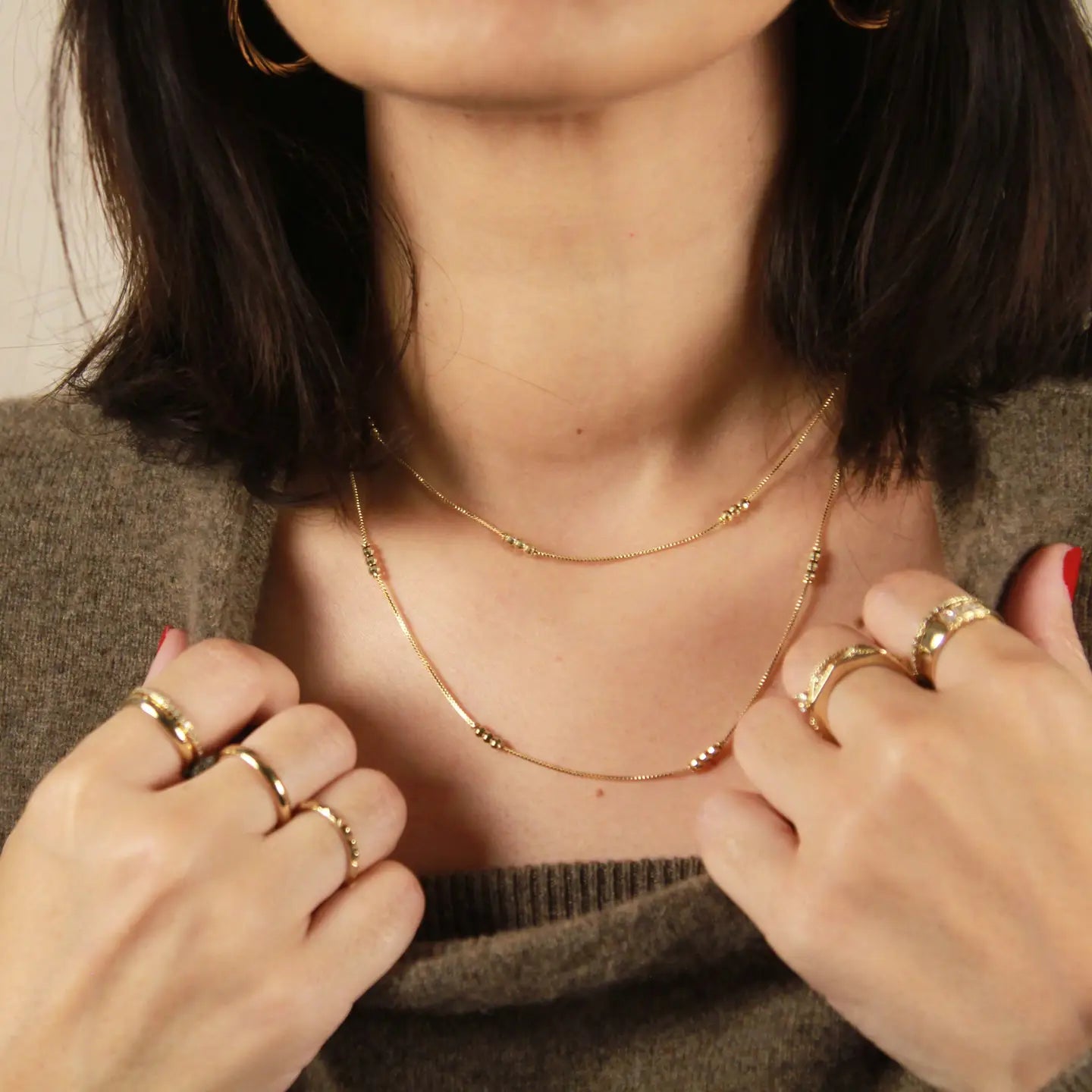 Woman wearing a gold necklace and multiple rings on a neutral background