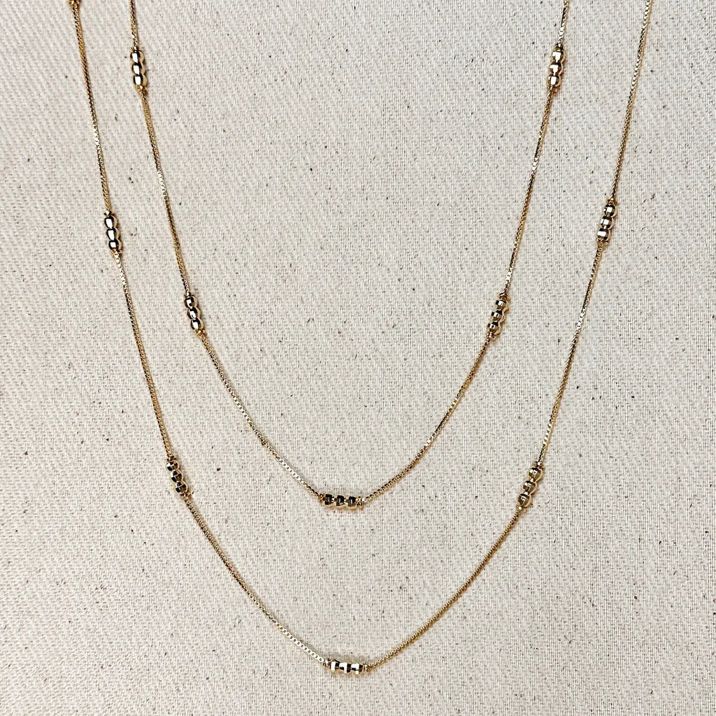 Two layered gold necklaces on a textured beige background
