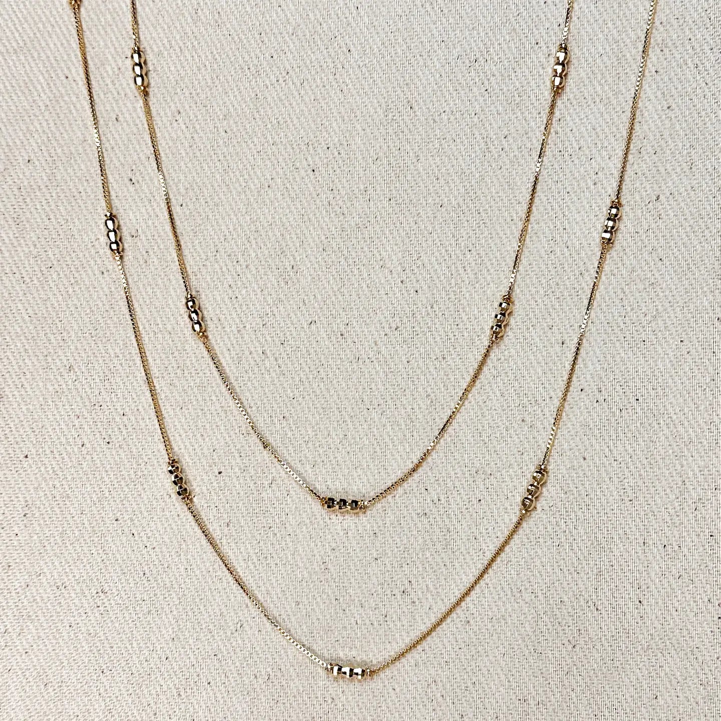 Two layered gold necklaces on a textured beige background