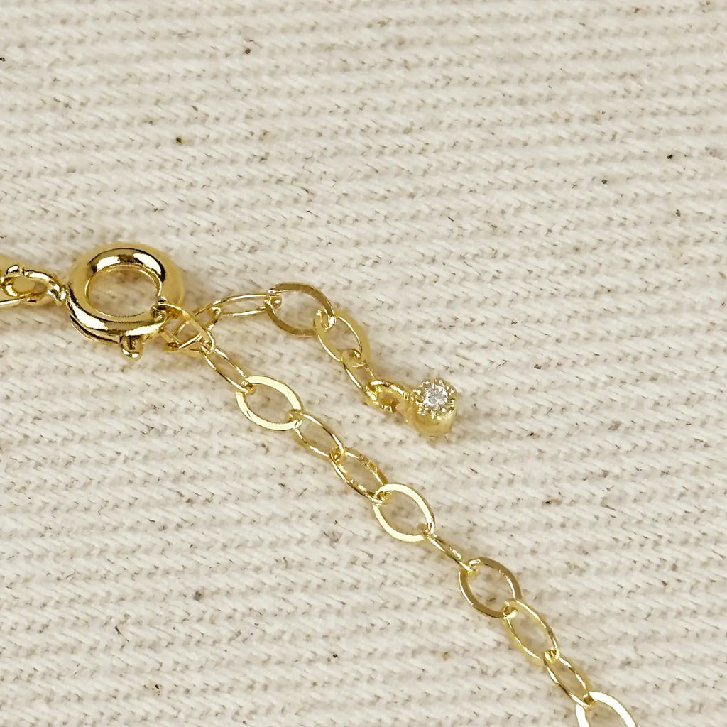 Gold chain bracelet with a clasp on a beige fabric background