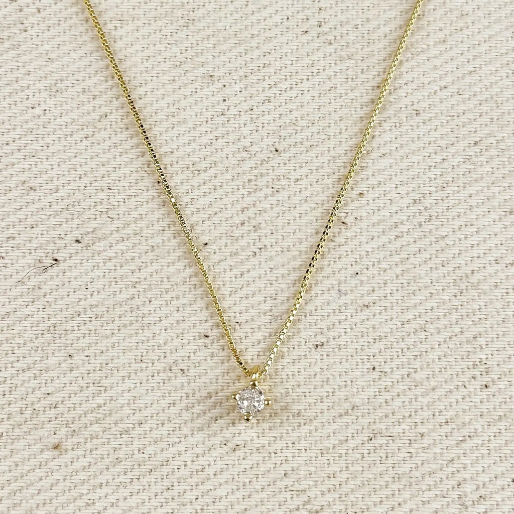 Gold necklace with a small diamond pendant on a textured beige background