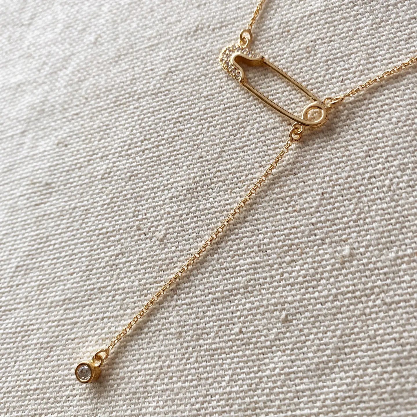 Gold necklace with a safety pin clasp on a textured beige background