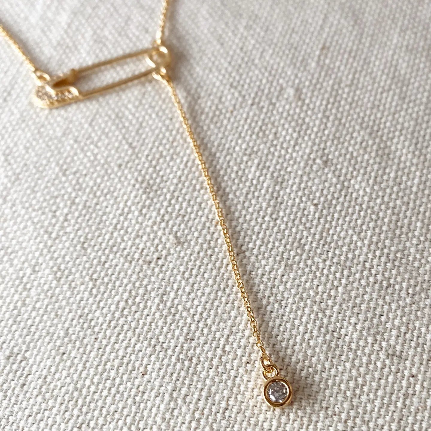 Gold necklace with a small pendant on a textured beige background