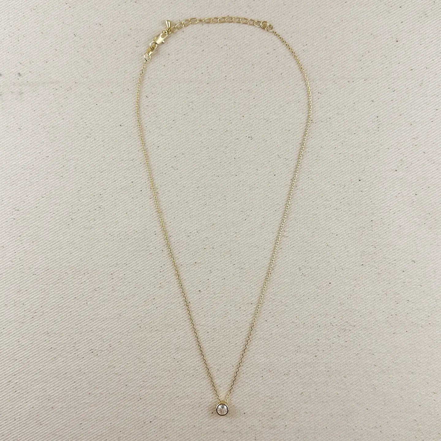 Gold necklace with a small pendant on a beige fabric background