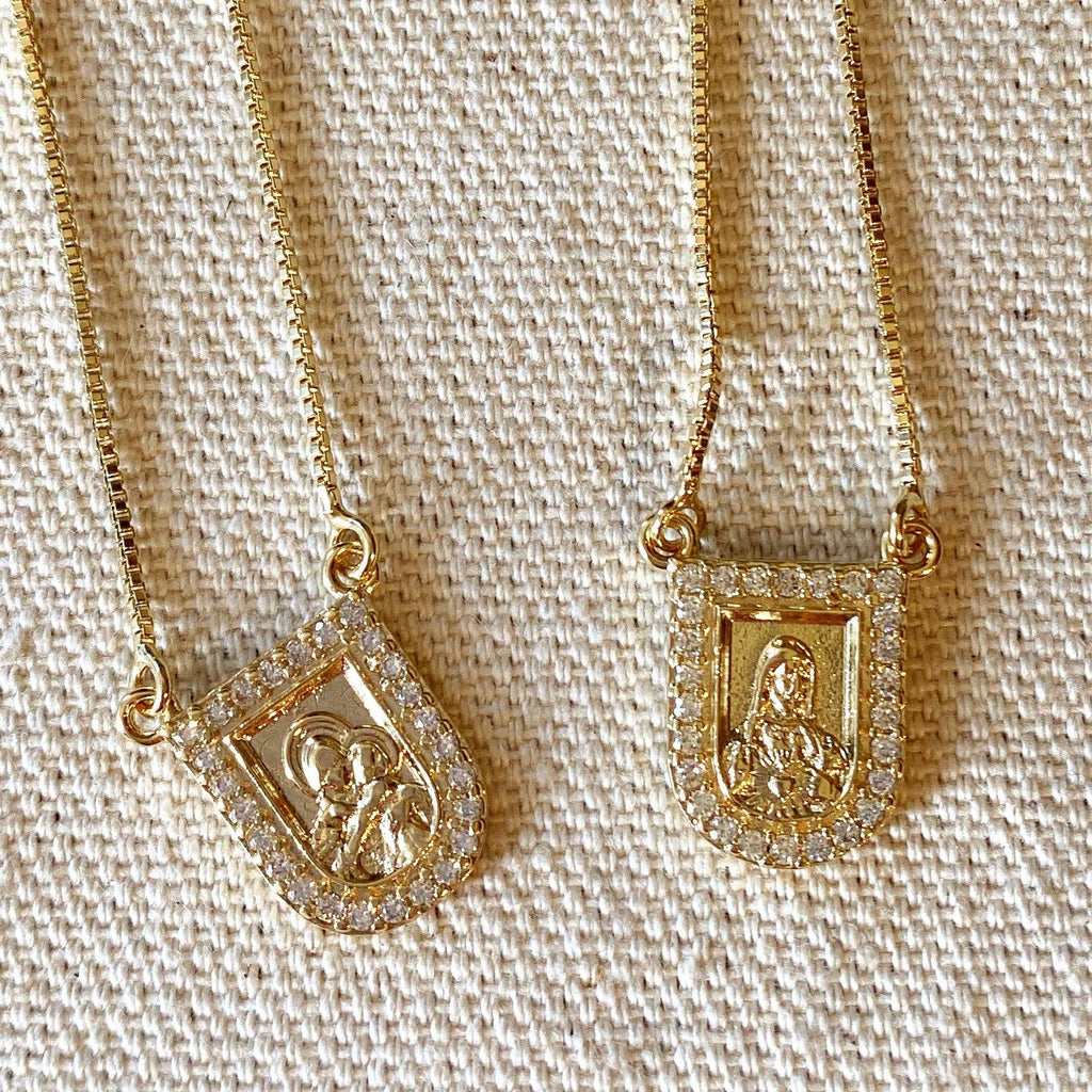 Two gold necklaces with religious-themed pendants on a textured beige background