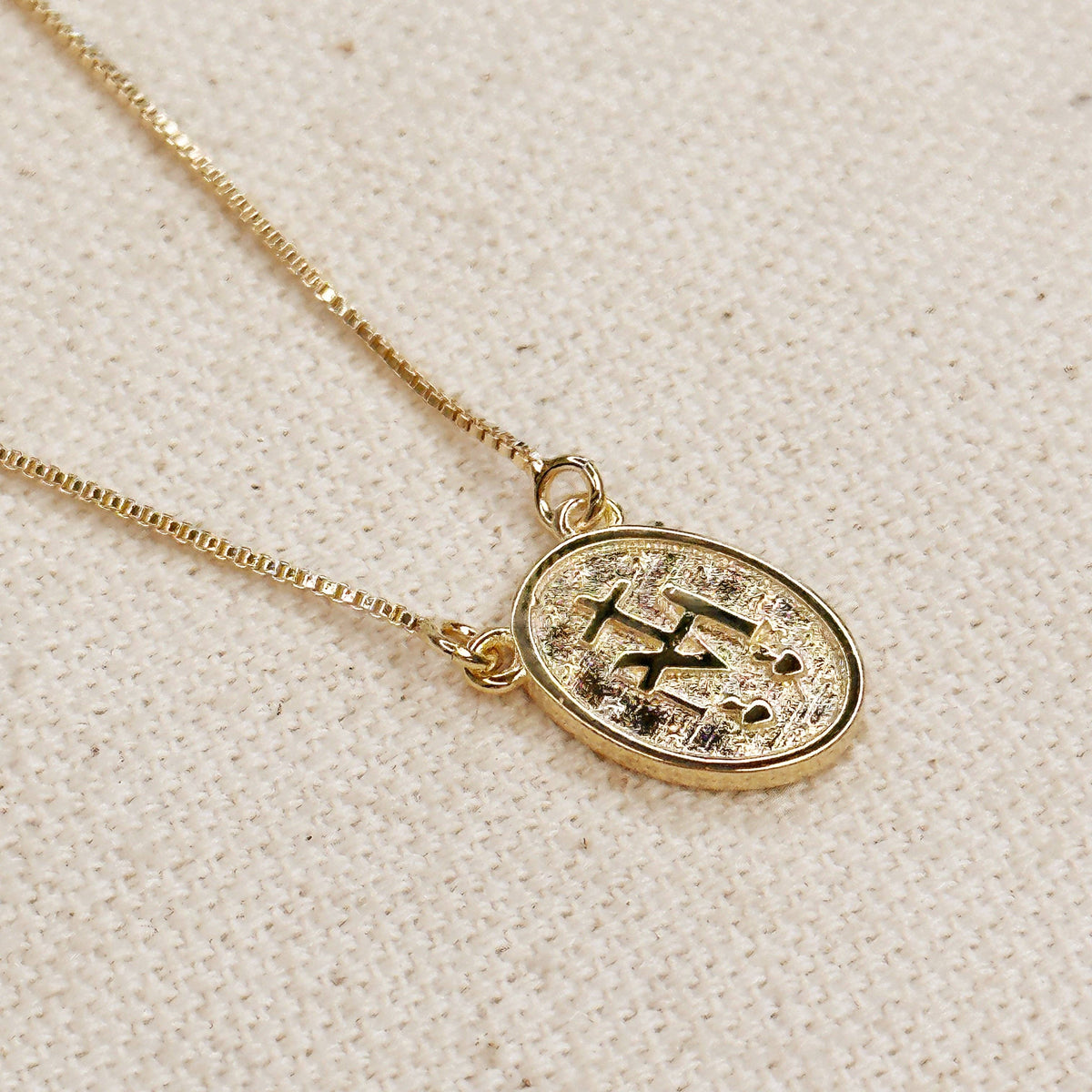 Gold necklace with a pendant on a textured beige background