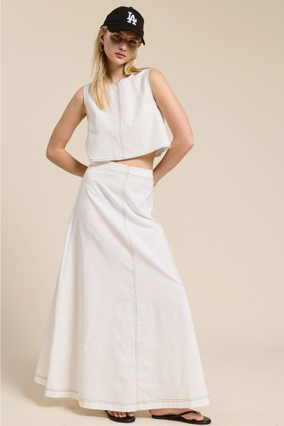 Woman wearing a white sleeveless top and skirt set with a cap on a beige background