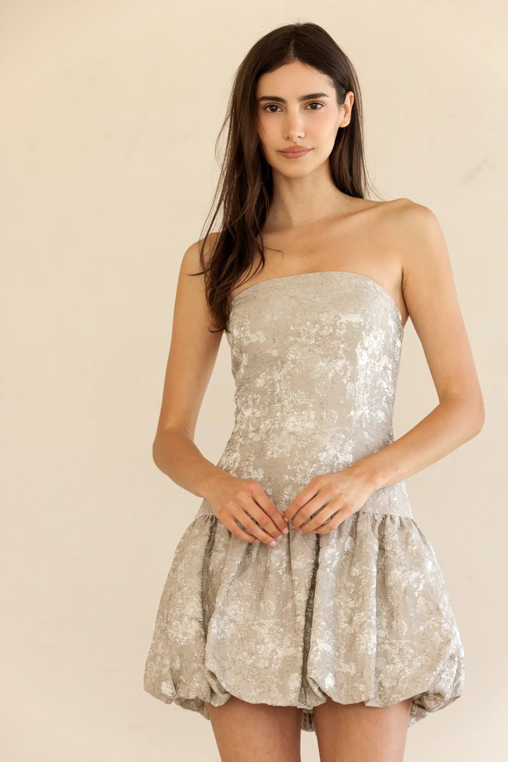 Woman wearing a strapless silver sequin dress against a beige background