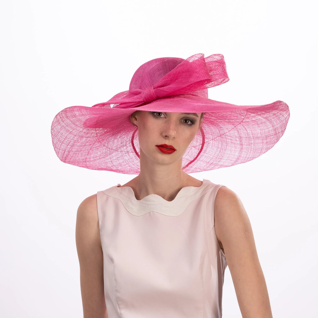 Model wearing a large pink hat with a white background