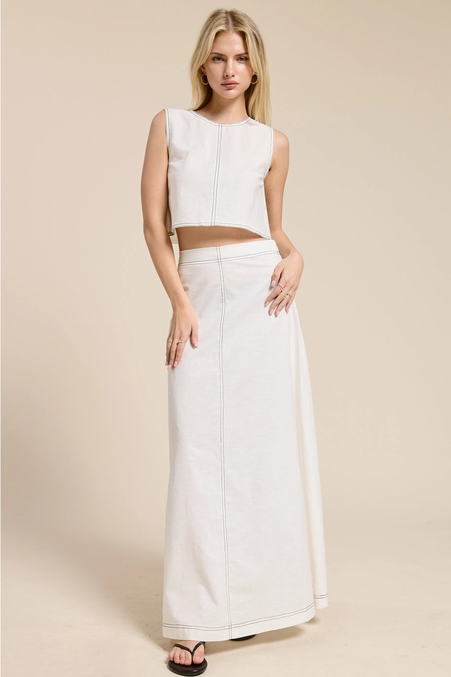 Woman wearing a white sleeveless top and long skirt on a beige background