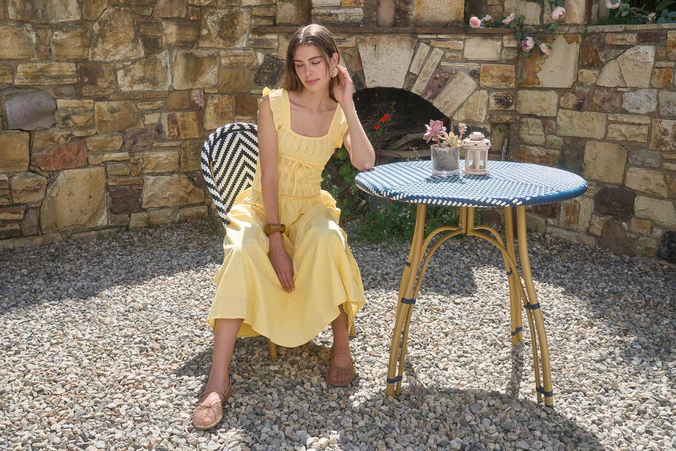 Woman in a yellow dress sitting at a small table outdoors against a stone wall.