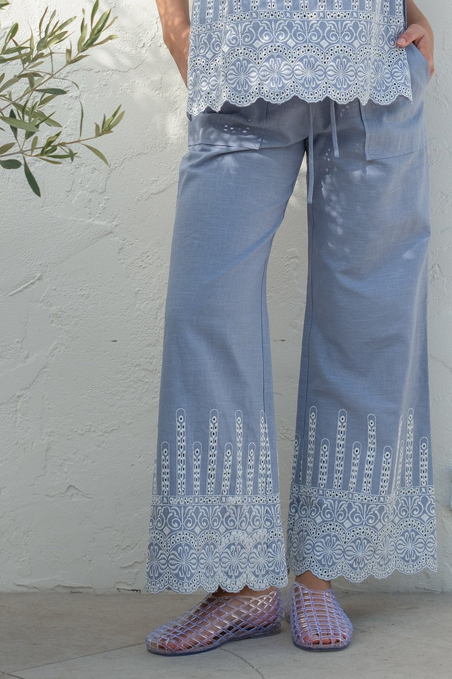 Person wearing light blue lace pants and a matching top against a white wall.