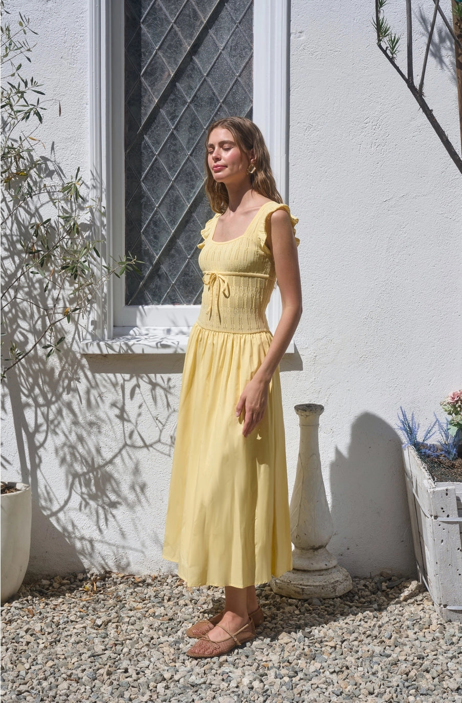 Woman in a yellow dress standing outdoors near a white wall with a window.