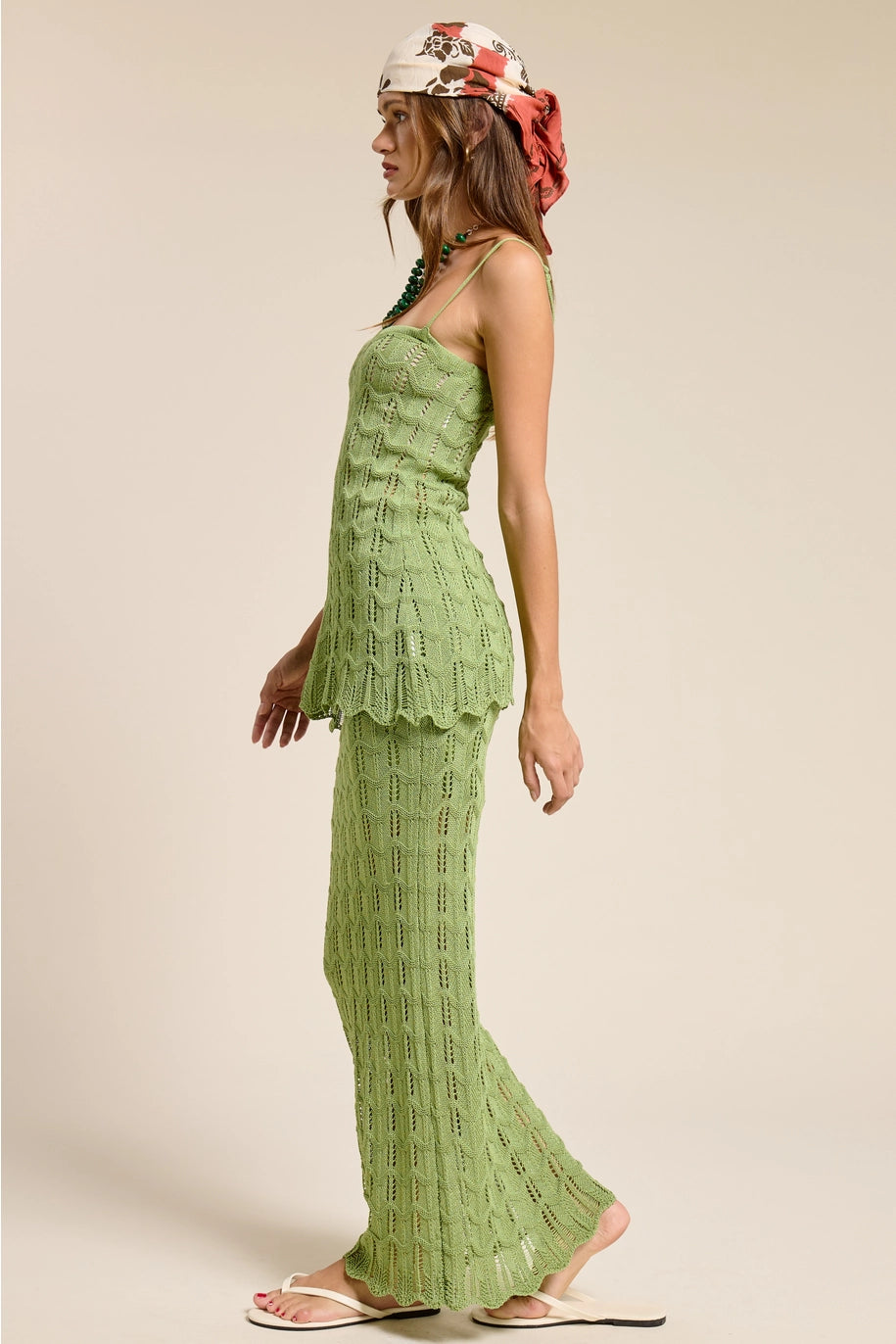 Woman wearing a green lace dress with a matching headscarf on a beige background