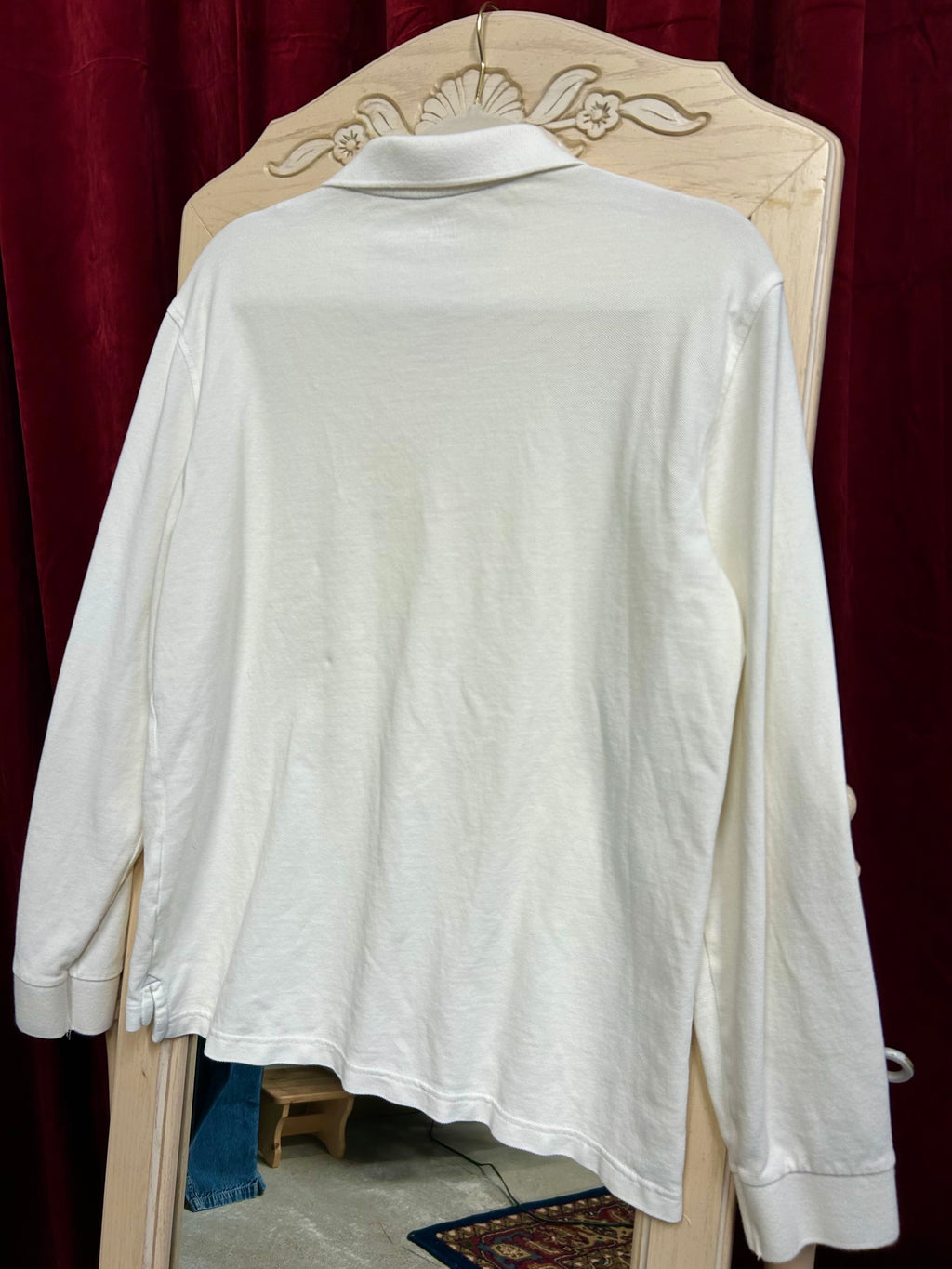 White long-sleeve shirt on a wooden hanger against a red curtain background