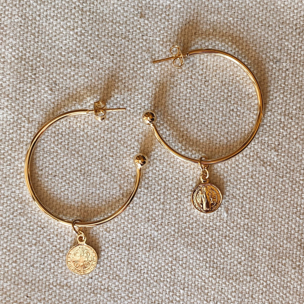 Gold hoop earrings with coin charms on a textured beige background