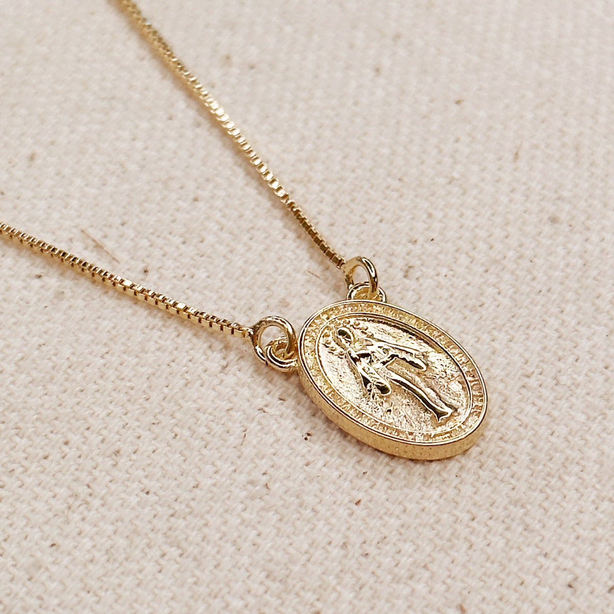Gold necklace with a religious pendant on a beige fabric background