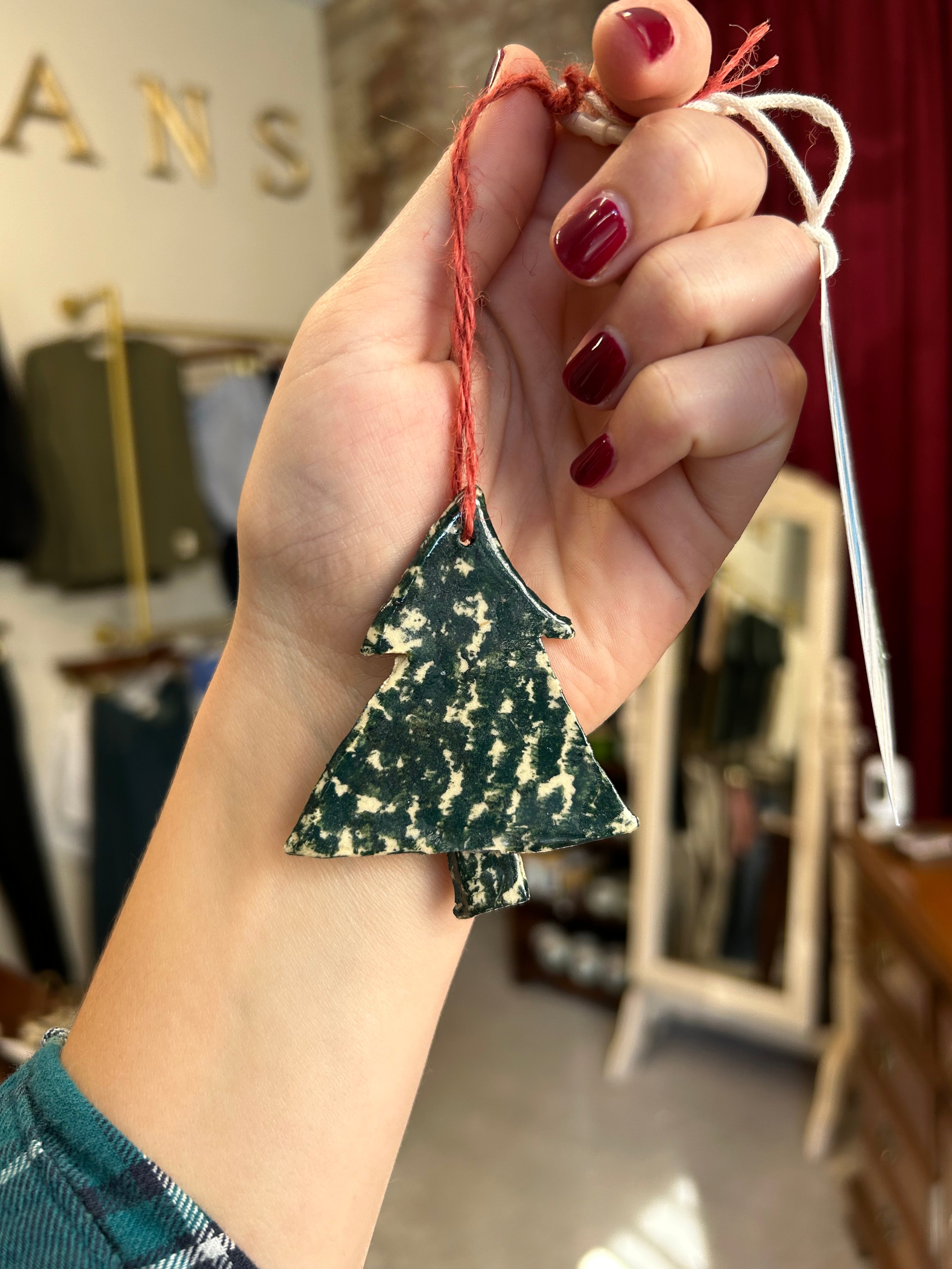 Hand holding a green and white patterned Christmas tree ornament with a blurred background