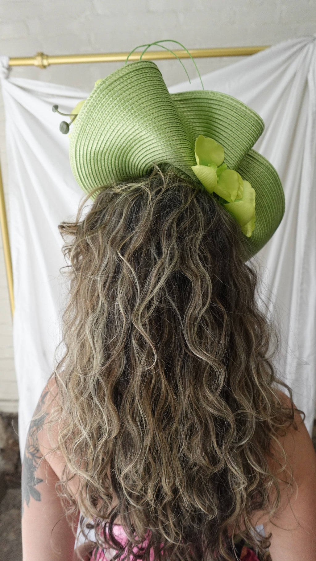 Close-up of a person wearing a green hat with a decorative bow, against a white background.