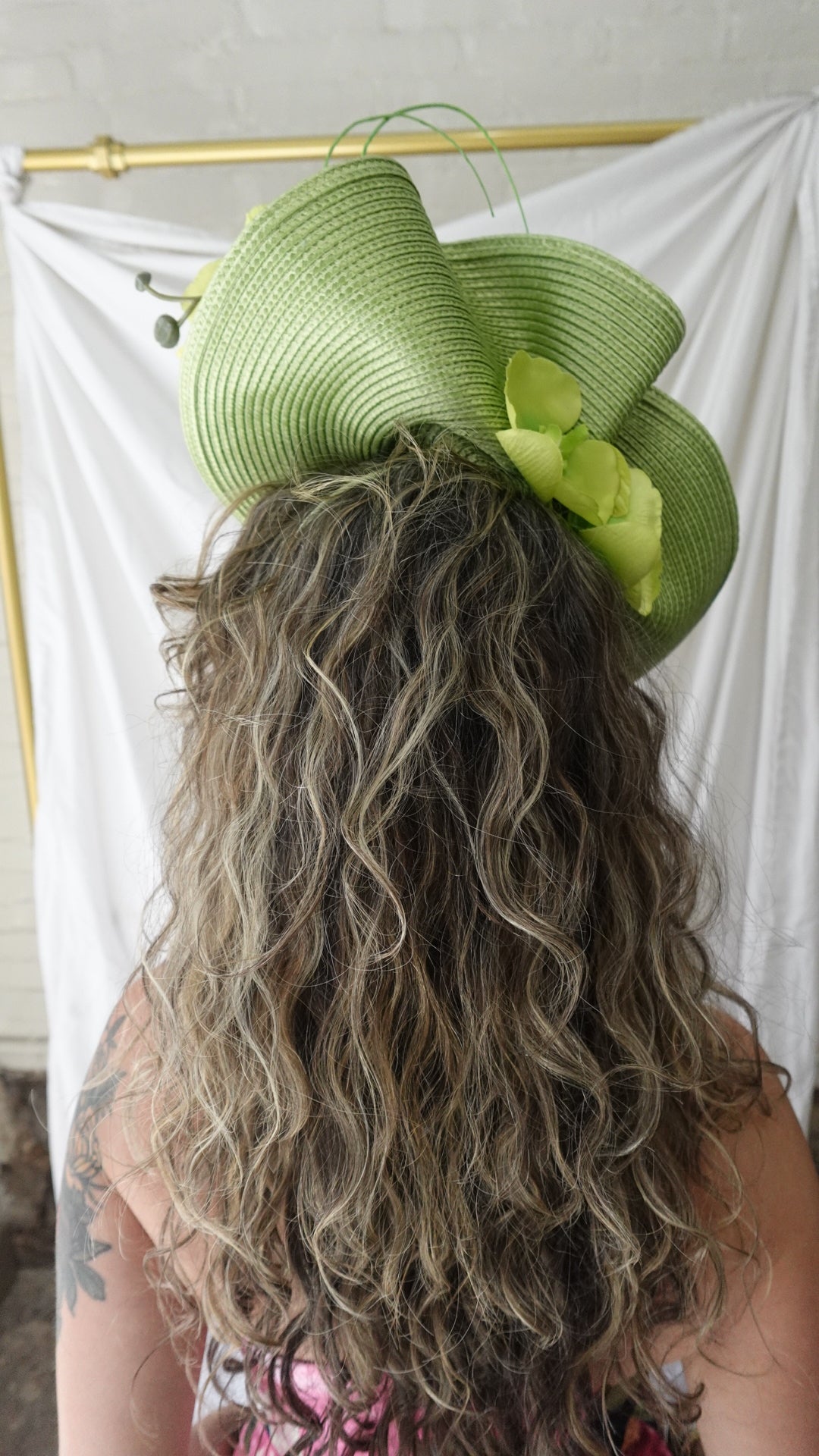 Close-up of a person wearing a green hat with a decorative bow, against a white background.