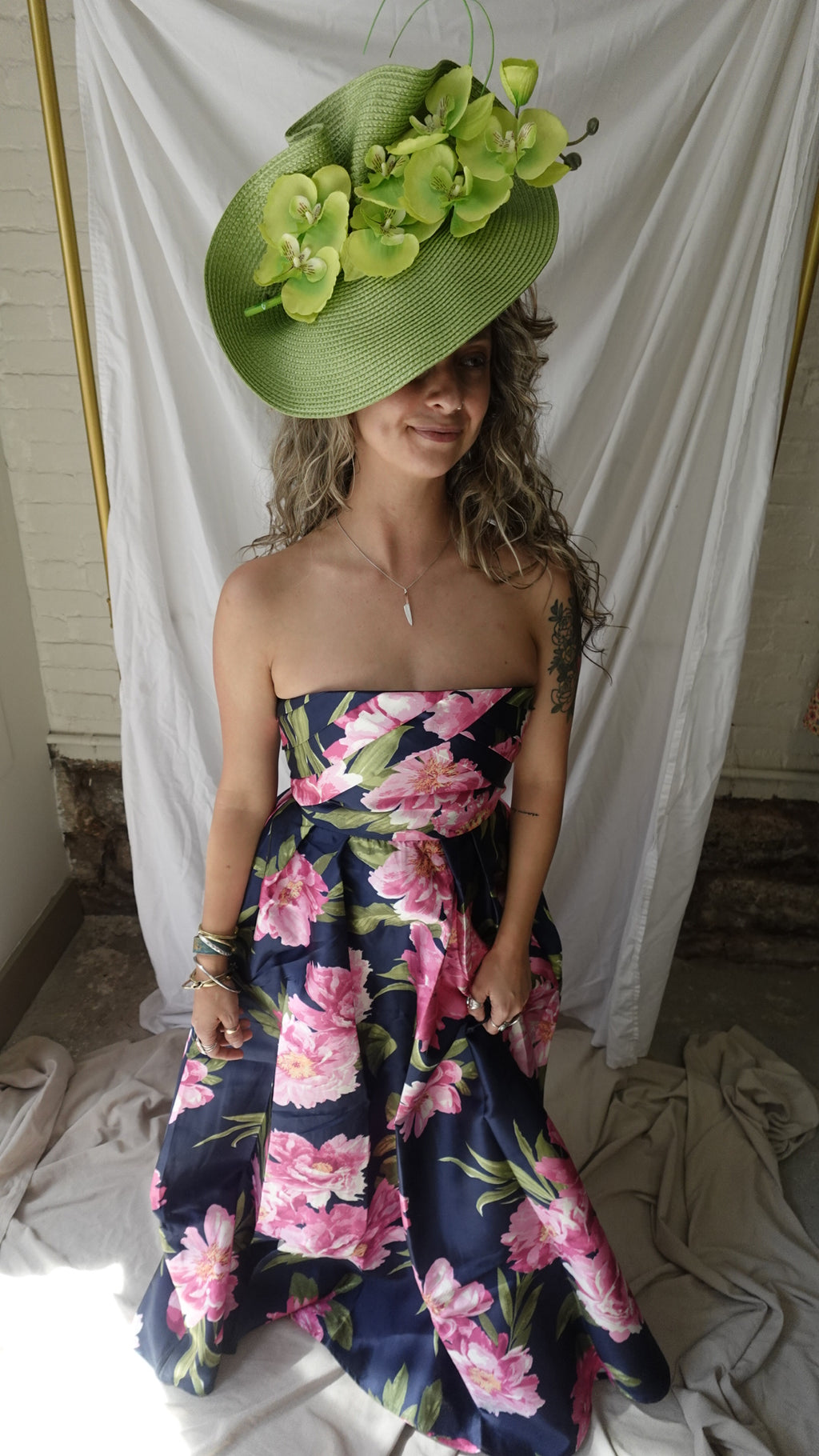 Person wearing a floral dress and green hat lying on a white sheet.