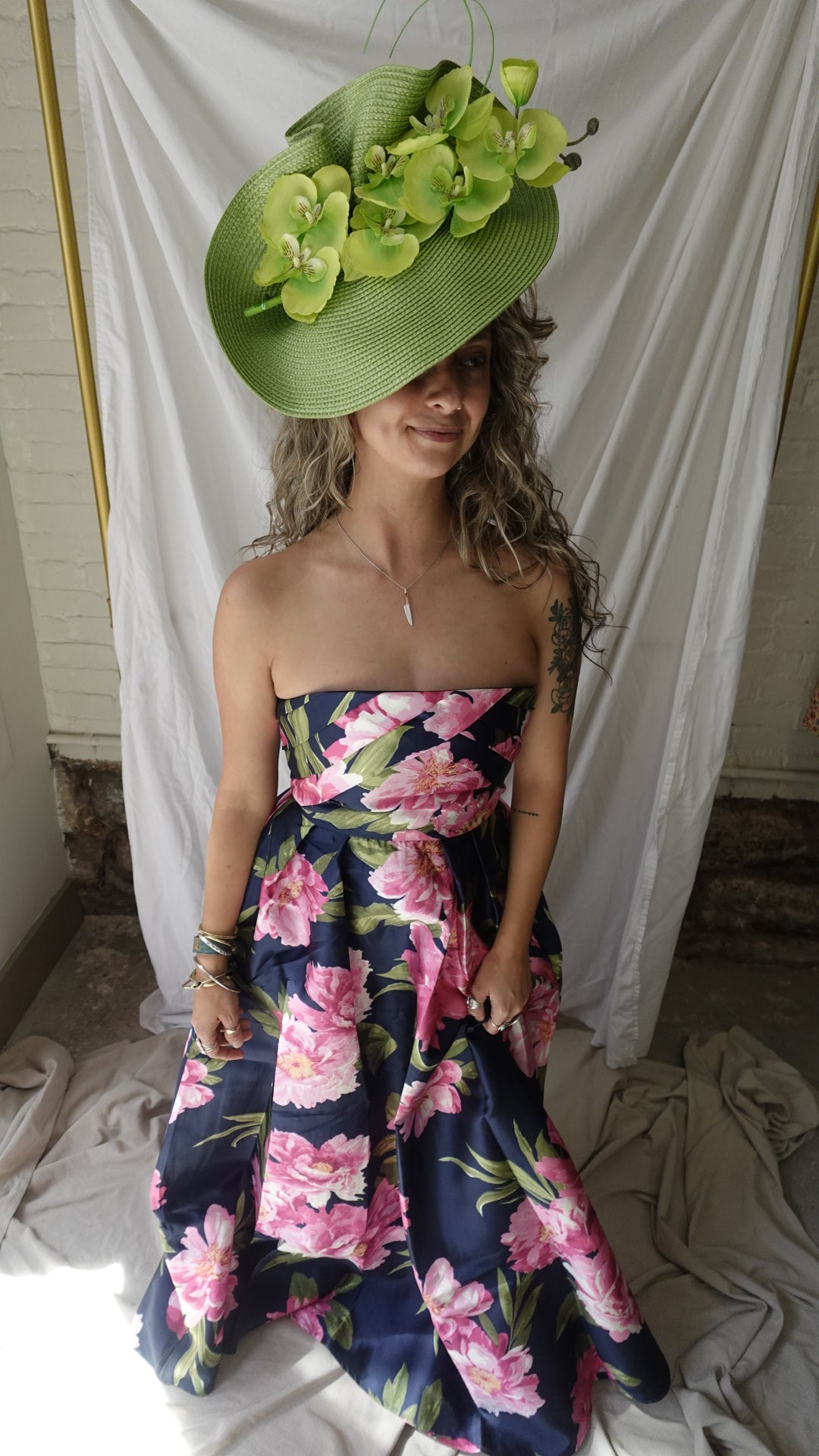 Person wearing a floral dress and green hat lying on a white sheet.