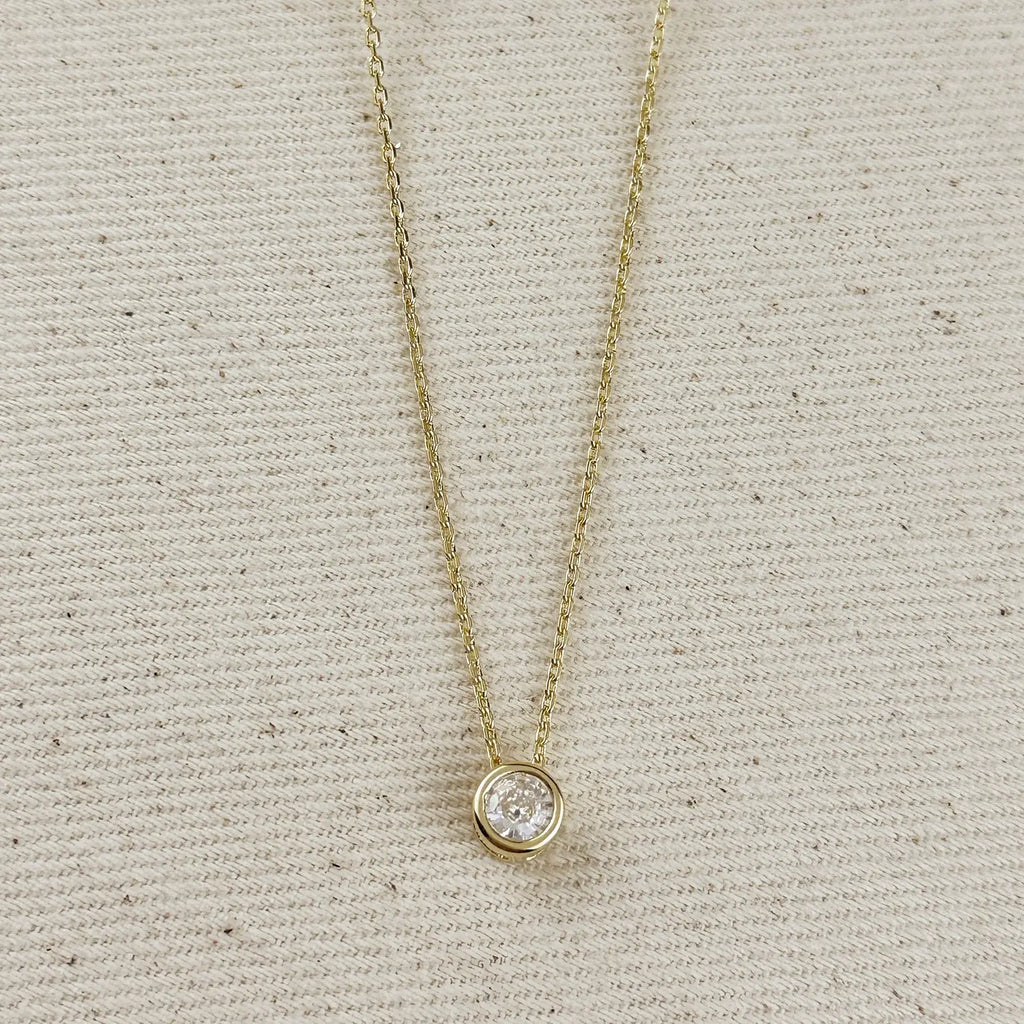 Gold necklace with a clear pendant on a textured beige background