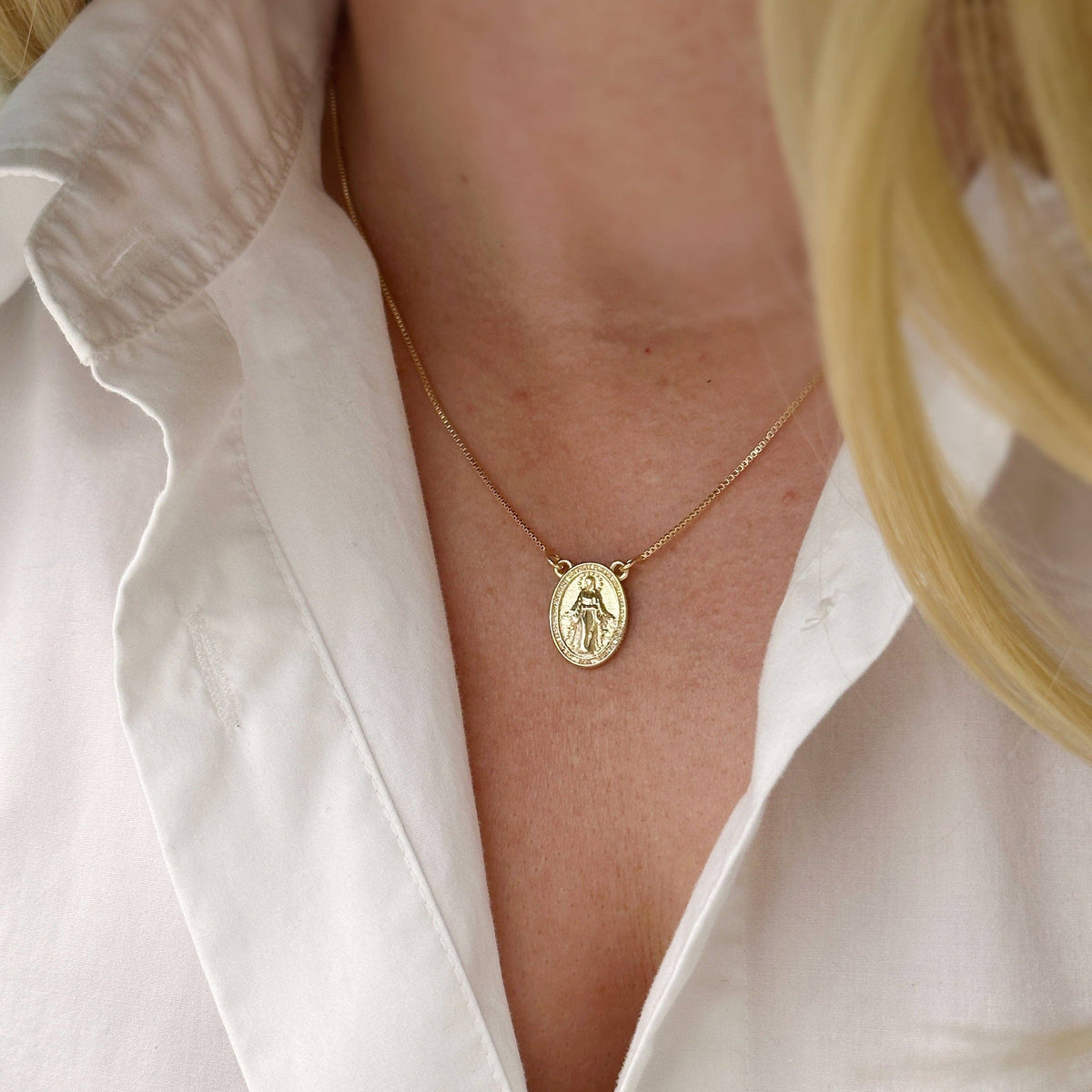 Gold necklace with a pendant worn by a person in a white shirt.