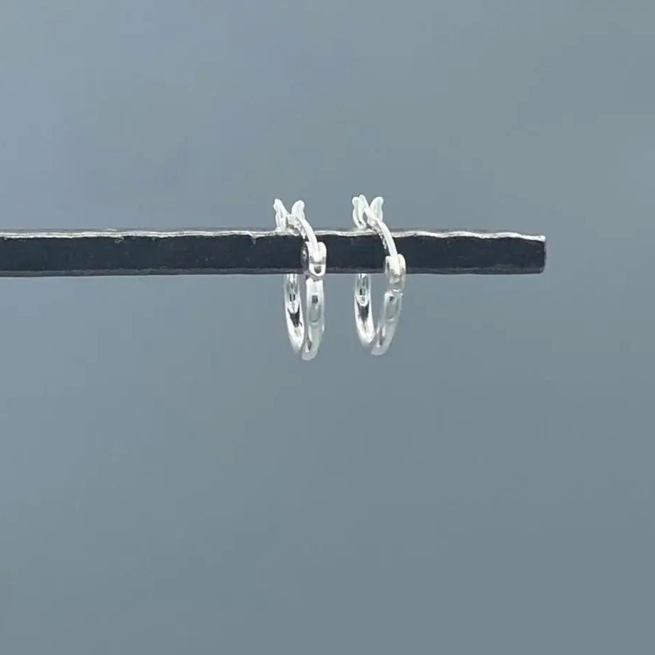 Small silver hoop earrings on a thin black rod against a gray background.
