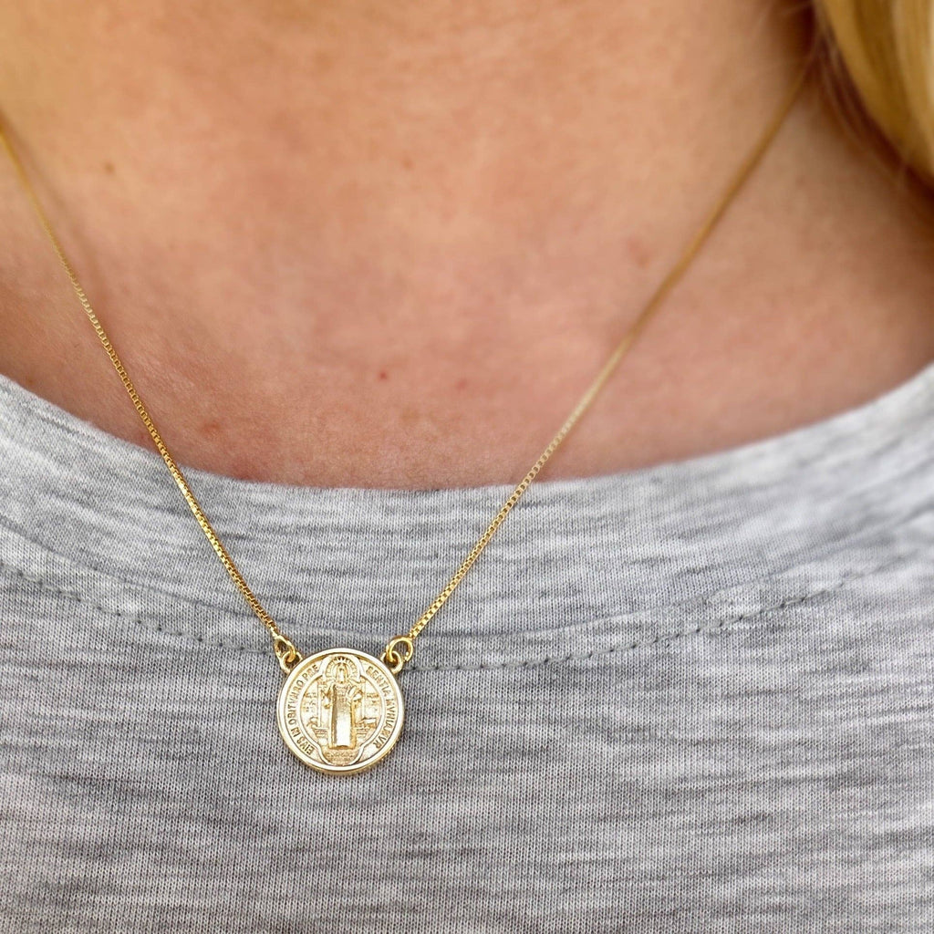 Gold necklace with a coin pendant worn by a person in a gray shirt.