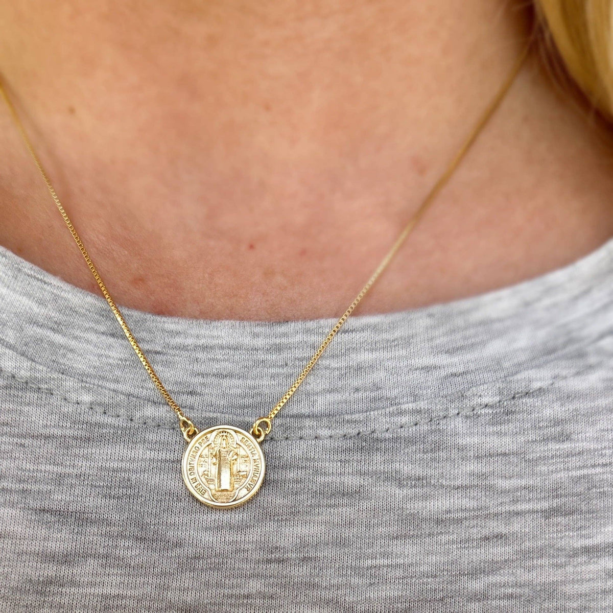 Gold necklace with a coin pendant worn by a person in a gray shirt.