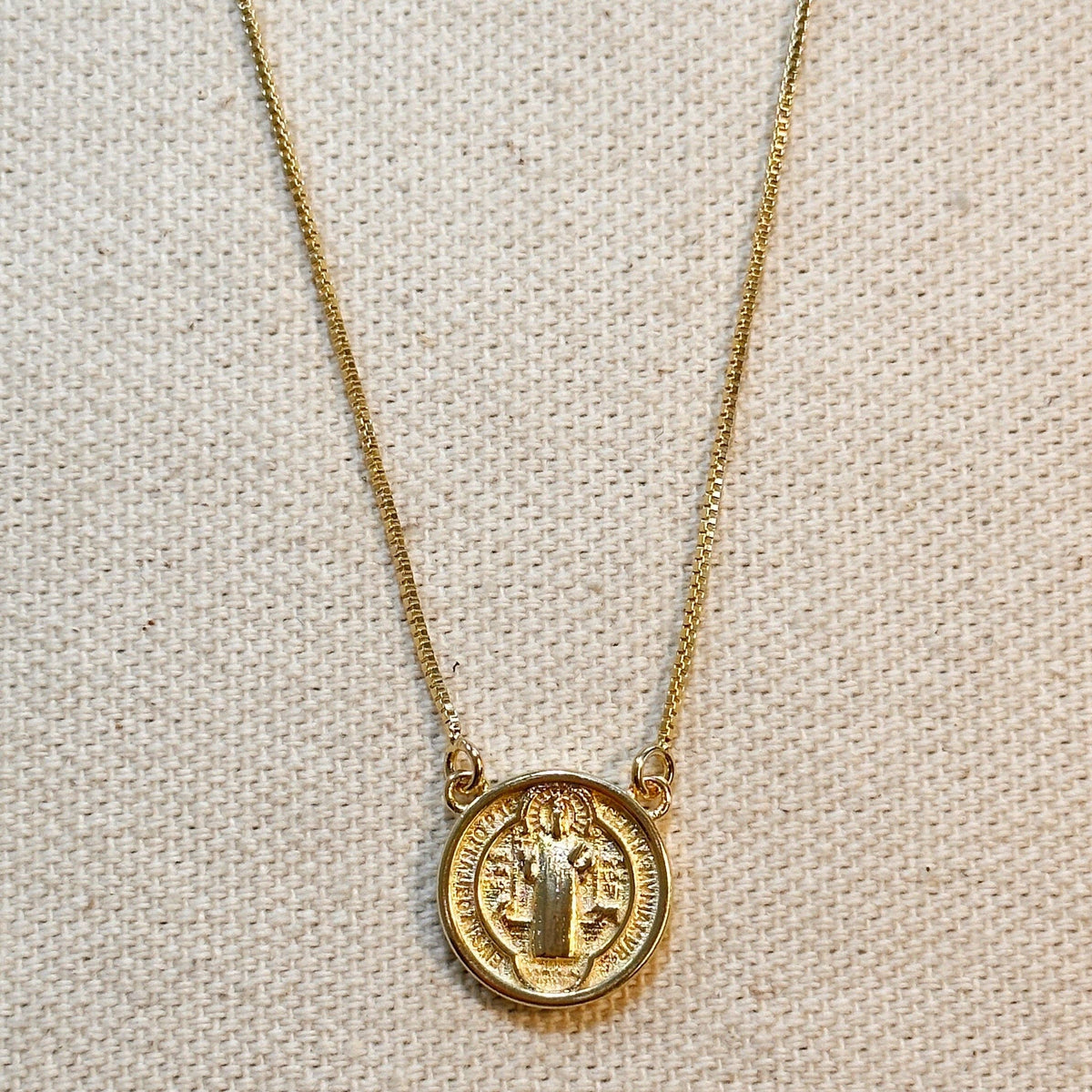 Gold necklace with a round pendant on a beige fabric background