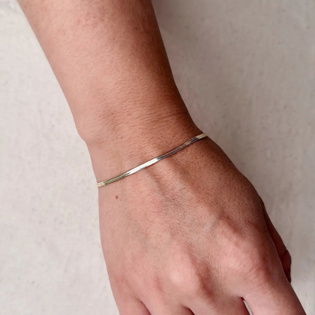 Silver bracelet on a wrist against a neutral background