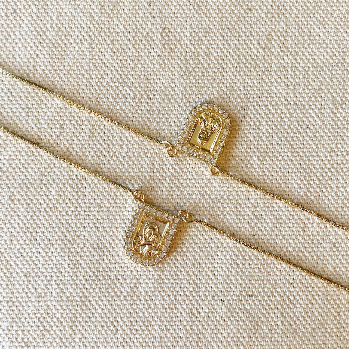 Gold necklaces with intricate pendants on a beige fabric background