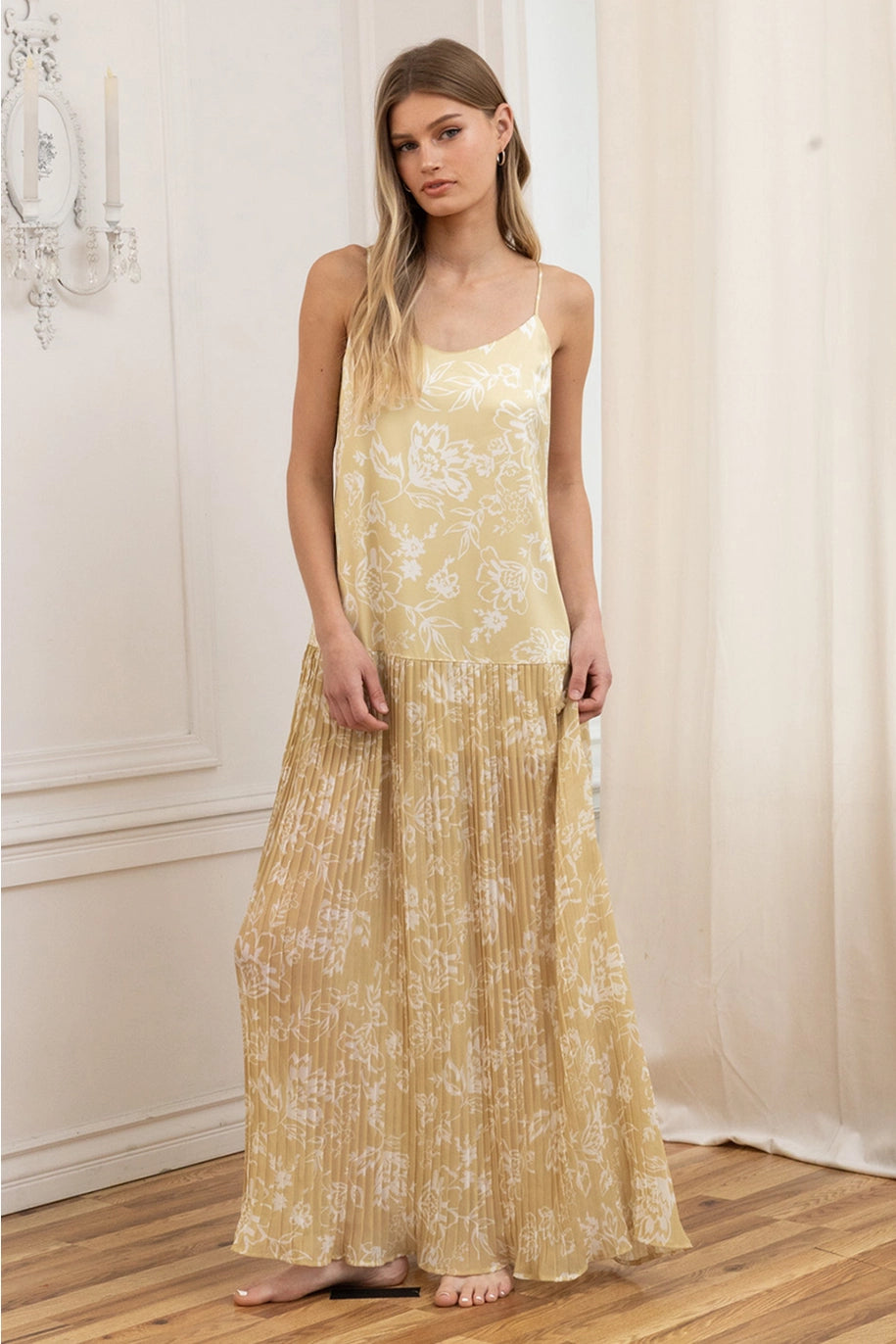 Woman wearing a yellow floral dress standing in a room with white walls and wooden floor.
