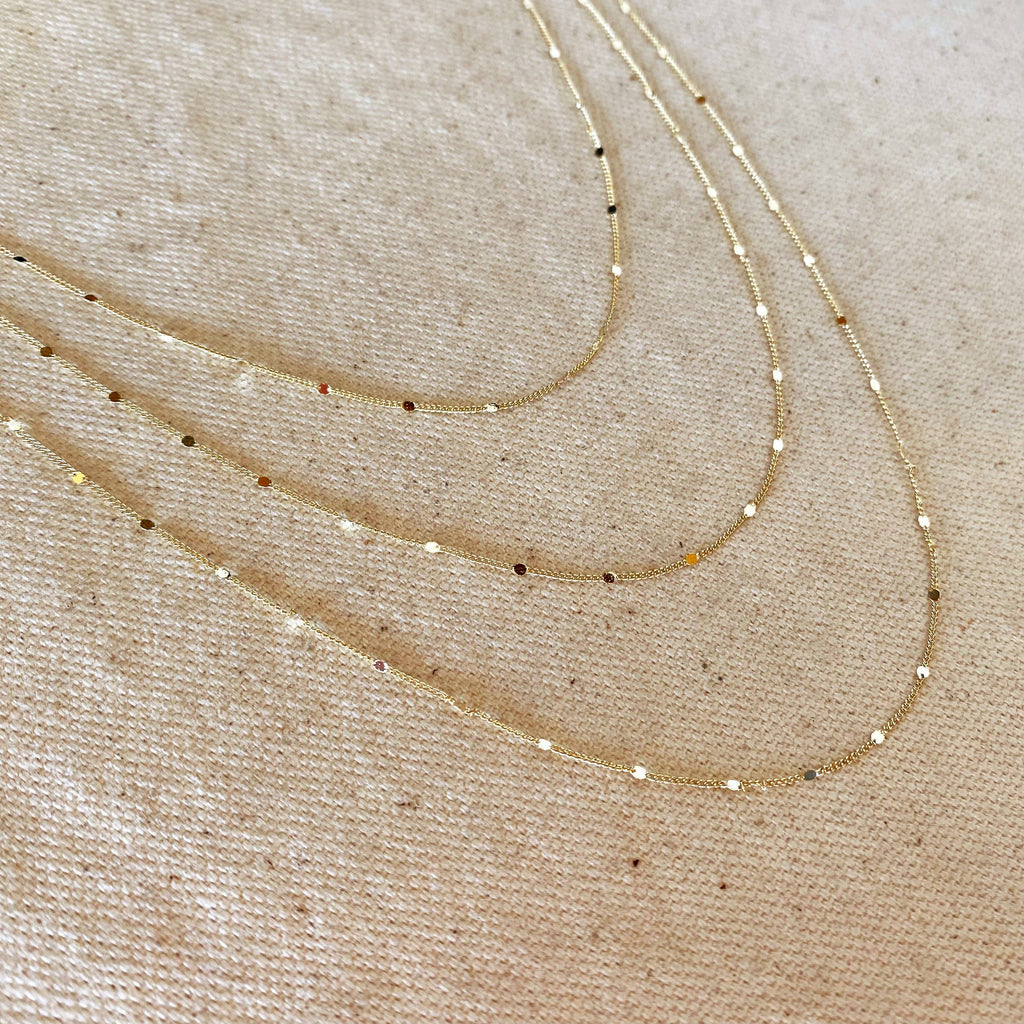Three gold necklaces on a beige fabric background