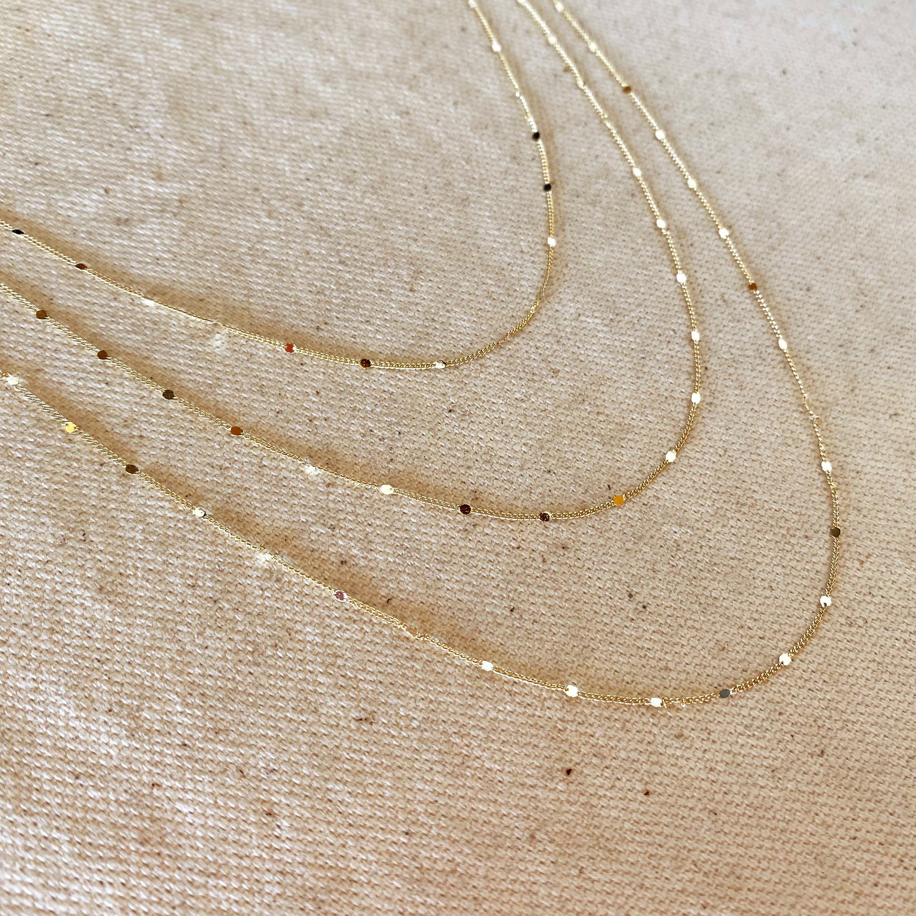 Three gold necklaces on a beige fabric background