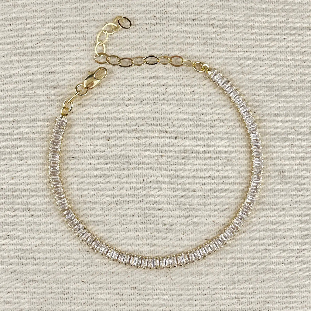 Gold bracelet with clear gemstones on a textured beige background