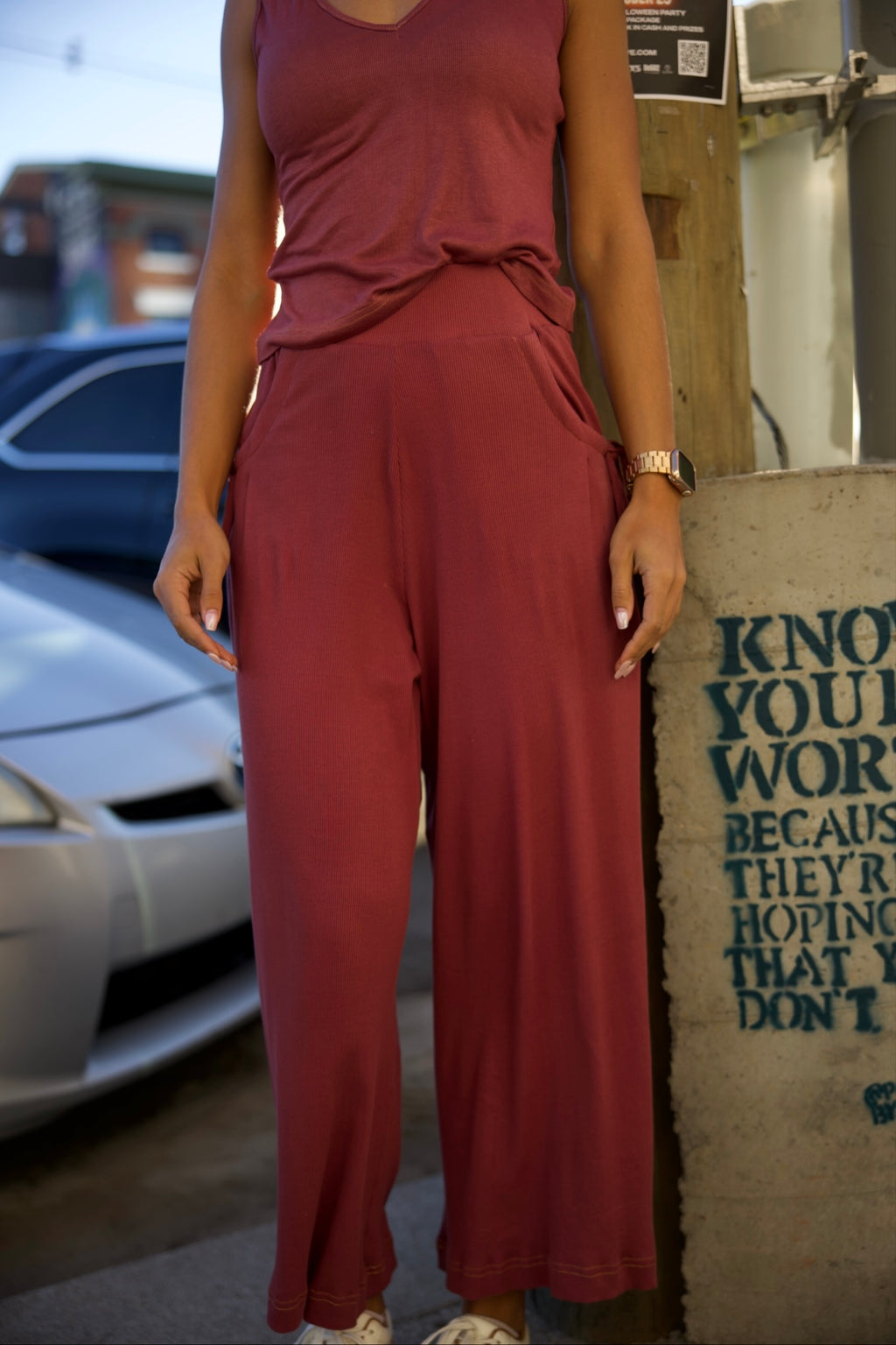 Person wearing a maroon outfit standing next to a wall with text.