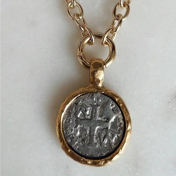 A gold chain necklace with a round pendant featuring an antique silver coin-like medallion with a cross design, set against a light gray background.