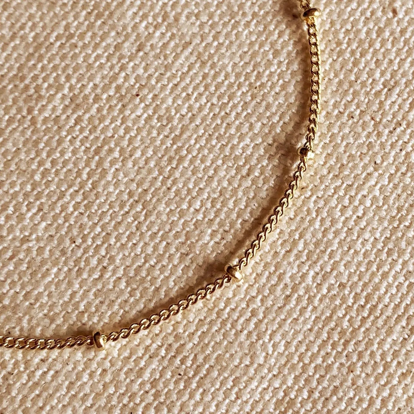 Gold chain necklace on a beige textured fabric background