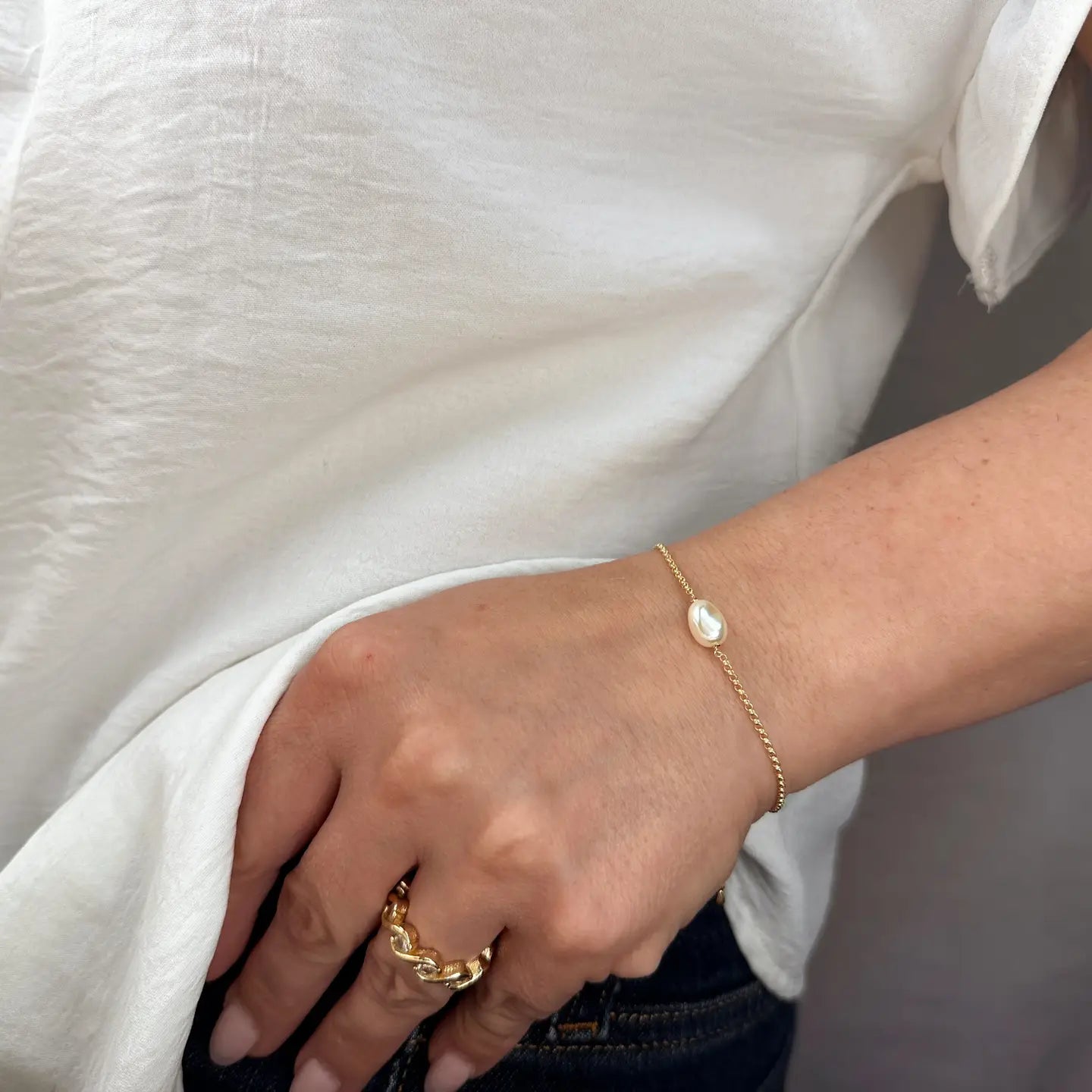 Hand wearing a gold ring and bracelet against a white background