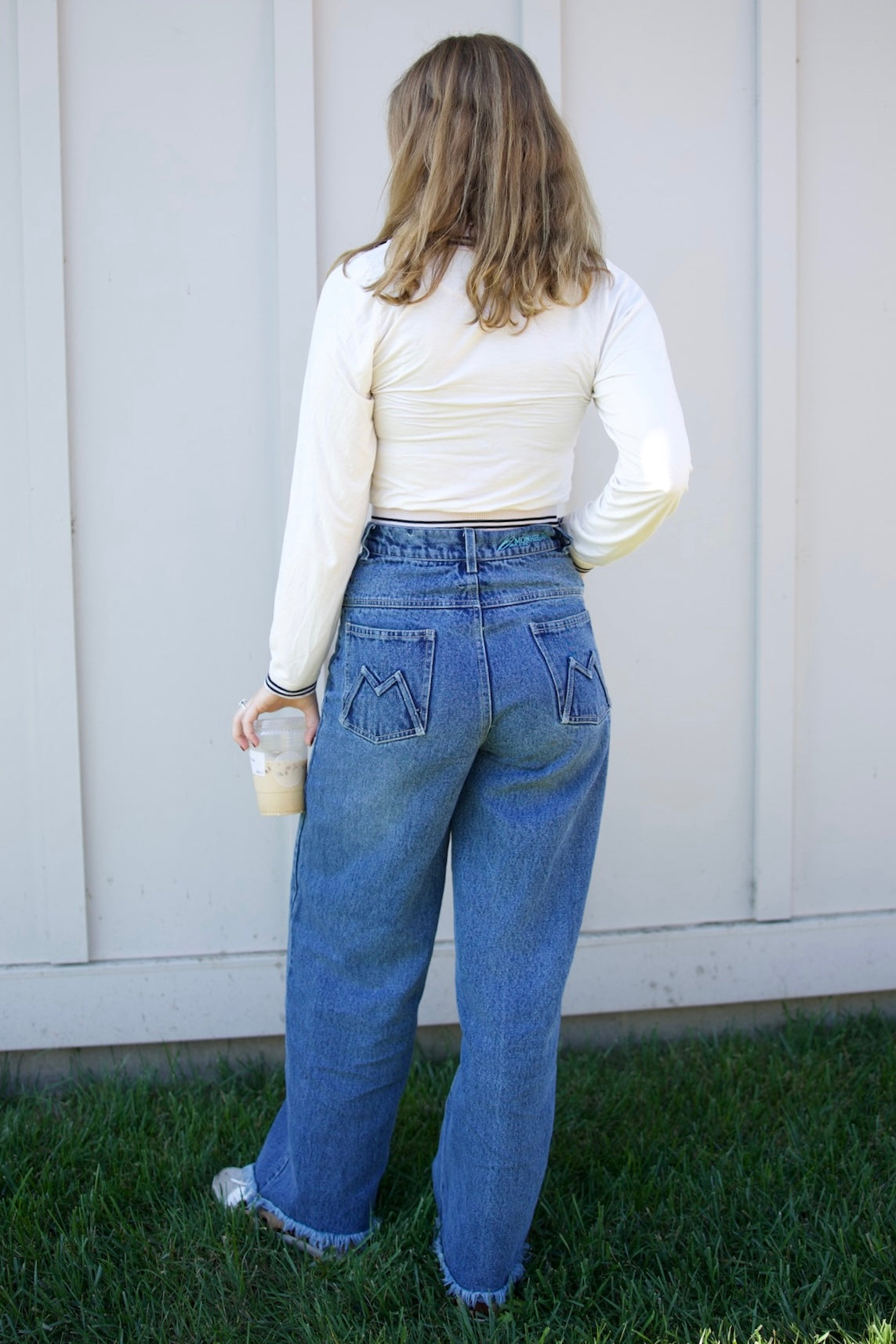 Person wearing blue jeans and a white long-sleeve shirt standing in front of a white wall.